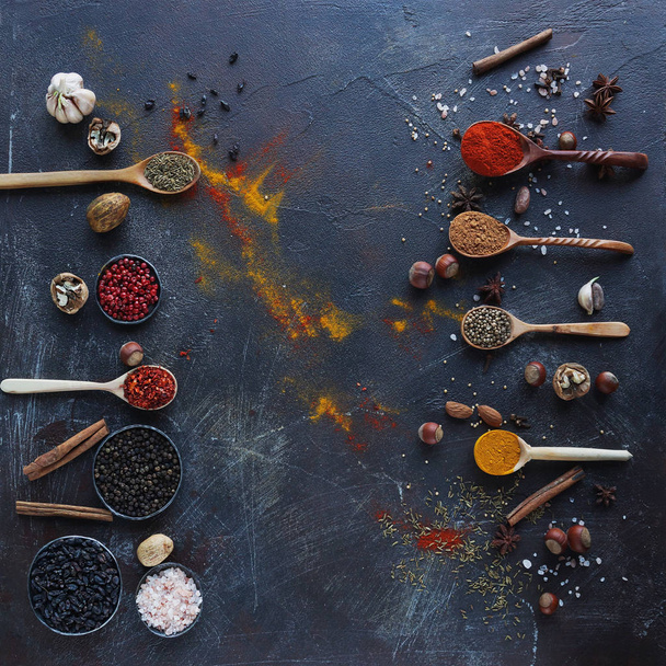 Various indian spices in wooden spoons, herbs and nuts on dark stone table. Colorful italian spices, top view. Organic food, healthy lifestyle, space for text, banner - Photo, Image