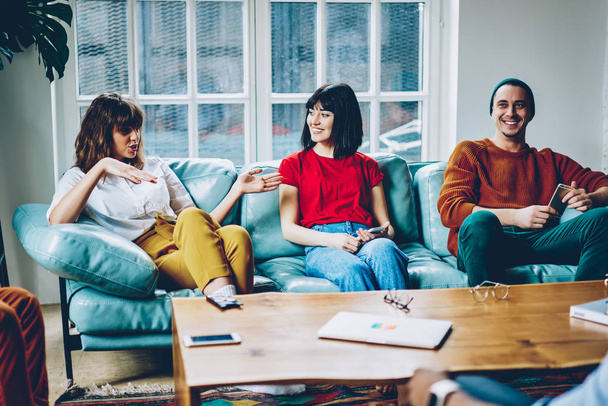 Hipster girl gesturing hands explaining information during game with friends in modern apartment.positive young people dressed in casual wear communicating with each other enjoying recreation time - Photo, Image