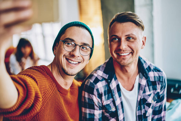 Cheerful young men dressed in casual wear smiling at camera while making selfie photo on front camera.positive hipster guys laughing and taking picture sitting in coworking - Fotoğraf, Görsel