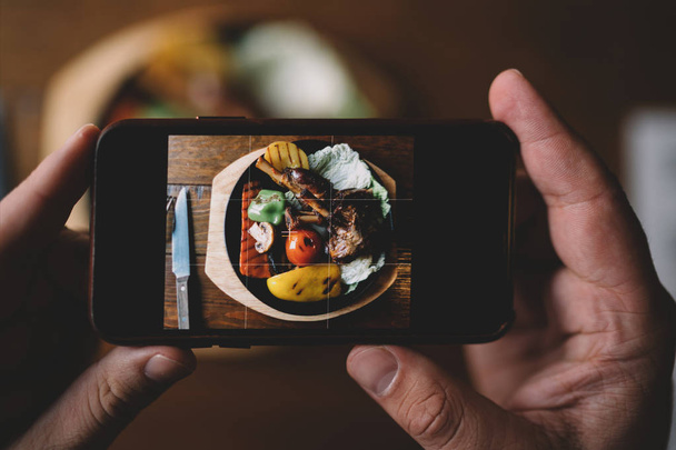 Food or technology concept. Man hands taking food photo by mobile phone. Close up of male hands holding modern smartphone, tasty dinner on the background. Toned image. Selective focus. - Foto, immagini