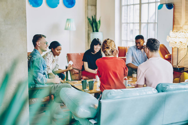 Multicultural young people playing games at table during friendly meeting in modern apartment with stylish interior.Diverse hipster guys enjoying entertainment together on weekend in flat - Photo, Image