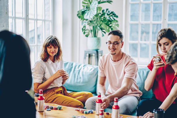 Young people dressed in casual wear enjoying game at table with chips and drink spending free time together in modern apartment.Hipster guys with cards playing poker in stylish flat - Photo, image