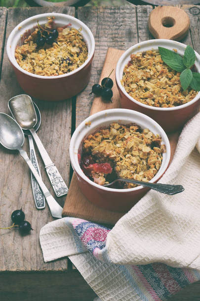 Fruits casserole or crumble with apples and black currant in red cup ramekin. Copy space. Berry and fruits dessert ready to eat. Homemade baking. Healthy pastries. Rustic photo. - Photo, Image