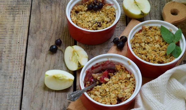 Fruits casserole or crumble with apples and black currant in red cup ramekin. Copy space. Berry and fruits dessert ready to eat. Homemade baking. Healthy pastries. Rustic photo. - Photo, Image