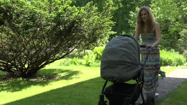 Matka v šatech se snaží poslat dítě spát v kočárku na zahradě. 4k - Záběry, video