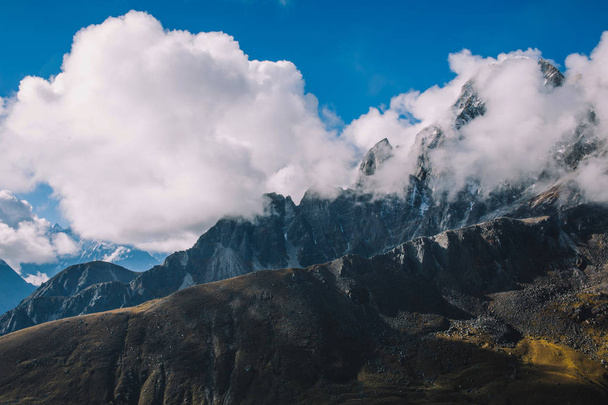 High mountains with snowy peaks in clouds with blue sky. Colorful landscape with beautiful rocks and dramatic cloudy sky. Nature background. Amazing mountains. Travel concept. Everest region, Nepal. - Photo, image