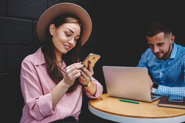 Pozytywne młoda kobieta śmiech i rozmowy na smartphone z przyjaciółmi za pomocą 4g Internetu, podczas gdy chłopak pracuje na freelance w komputerze przenośnym w kawiarni. Kobiece bogger wiadomości na telefon - Zdjęcie, obraz
