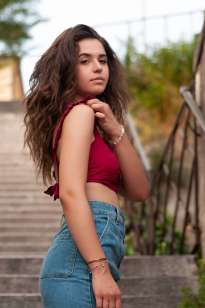 Close-up of beautiful young girl, with red bodice, looks at the camera. Close-up of expressions of young beautiful girl on some steps outside. - Foto, imagen