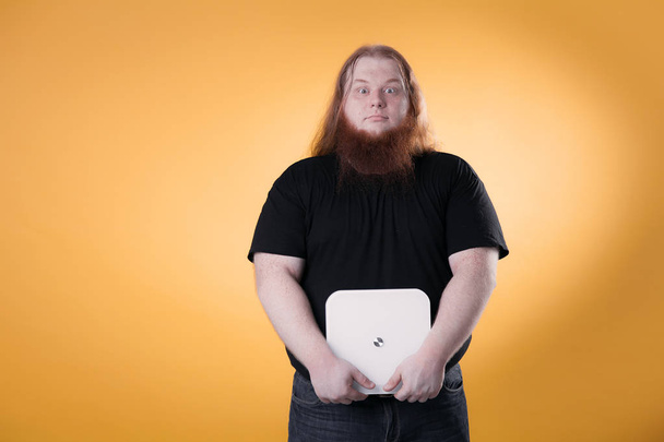 A fat man is holding a scales. A big red-haired bearded guy. - Photo, Image