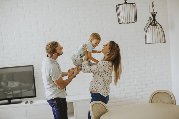 Молодая счастливая семья обнимается в комнате
 - Фото, изображение