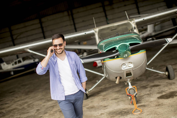 Joven piloto joven guapo comprobar avión en el hangar y el uso de teléfono móvil
 - Foto, imagen