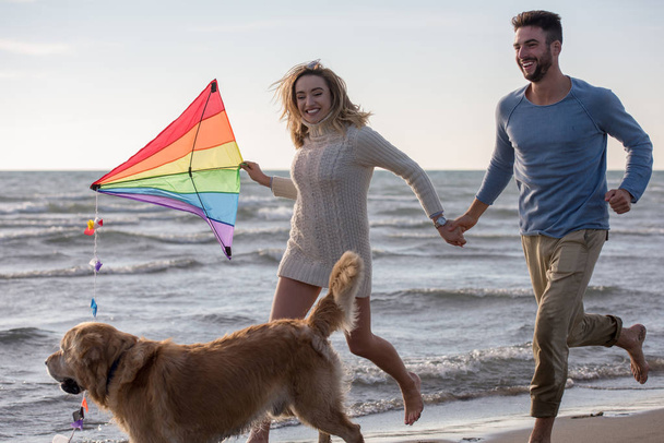 Young Couple having fun playing with a dog and Kite on the beach at autumn day - Photo, Image