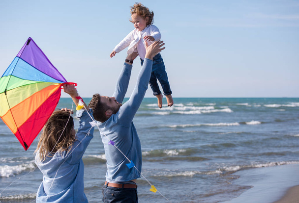 young family with kids resting and having fun with a kite at beach during autumn day - Foto, Imagen