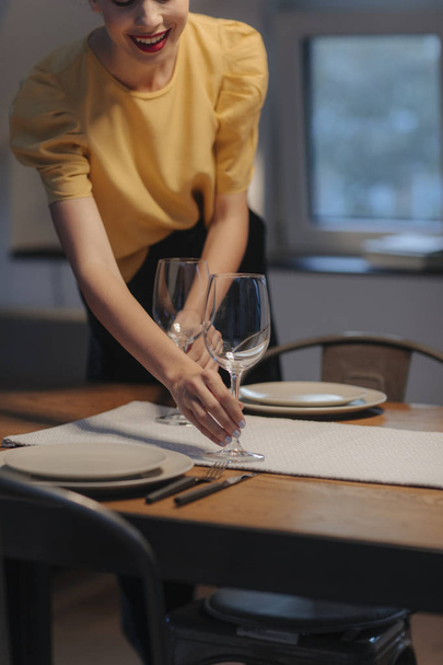Beautiful young woman setting up table for dinner party at home. - Foto, afbeelding