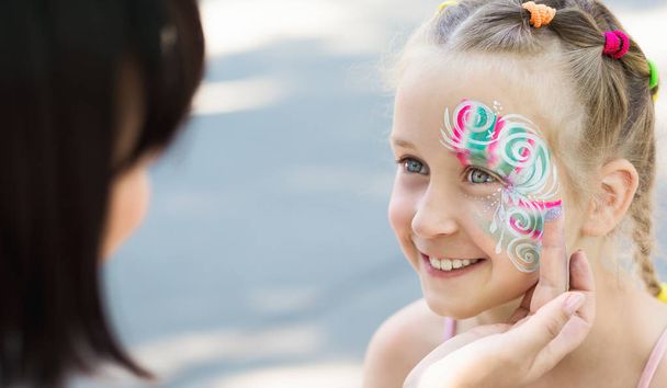 Little girl getting her face painted by face painting artist. - 写真・画像