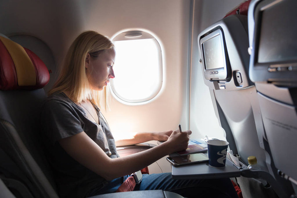 Gelegenheitsfrau, die in einem kommerziellen Passagierflugzeug fliegt und das Einwanderungsformular ausfüllt. - Foto, Bild