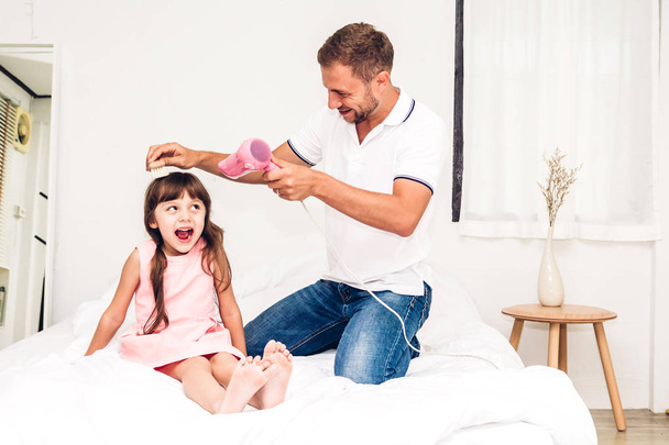 Apa kicsi lánya haj szárítás, és játszik együtt az ágyban otthon. Szeretet, család és az apa nap koncepció - Fotó, kép