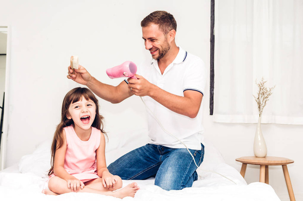 Pai secando cabelo pequena filha e brincando juntos na cama em casa. Amor da família e conceito do dia do pai
 - Foto, Imagem