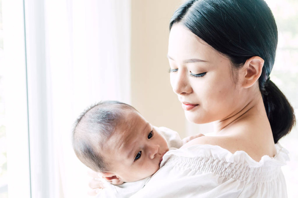Mother holding baby in her arms in a white bedroom.Love of family concept - Photo, Image