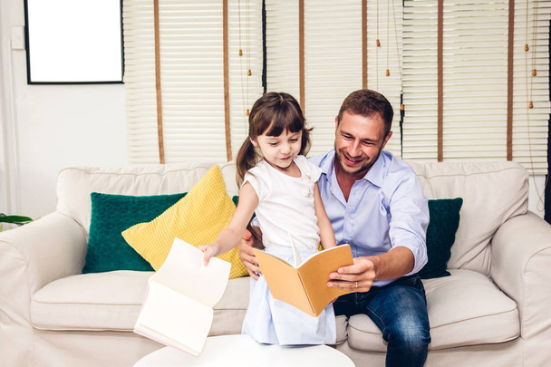 Father with little daughter having fun and read the book together on the sofa at home.Little girl and daddy enjoying with story book.Love of family and concept - Photo, image