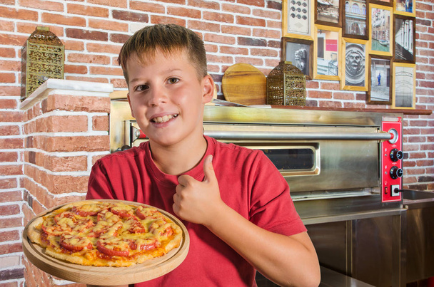 joyful teenager and pizza in his hand on a wooden board in cafe - Photo, Image