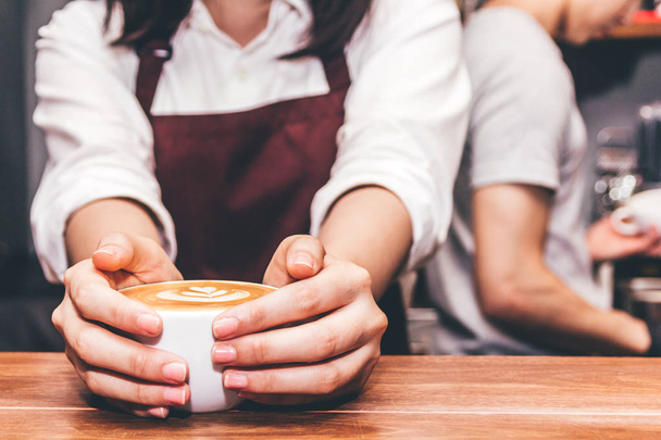 Женщина-бариста держит и дает кофе латте искусство для клиента на деревянном столе в кафе
 - Фото, изображение