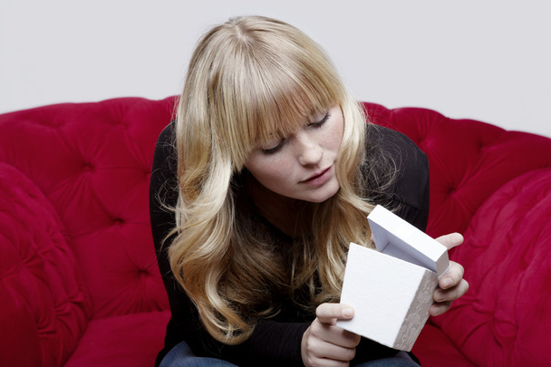 joven chica rubia con caja de regalo en sofá rojo delante de
 - Foto, imagen