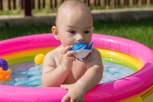 Ένα μικρό παιδί κάνει μπάνιο σε μια πισίνα, φουσκωτή παιδική πισίνα το καλοκαίρι - Φωτογραφία, εικόνα