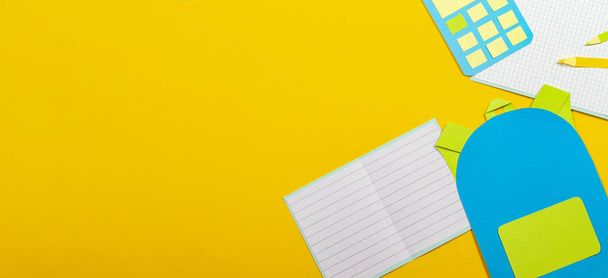 Formação escolar fundo de corte de papel. Mochila escolar, cadernos lápis calculadora papel cortado no fundo amarelo
 - Foto, Imagem
