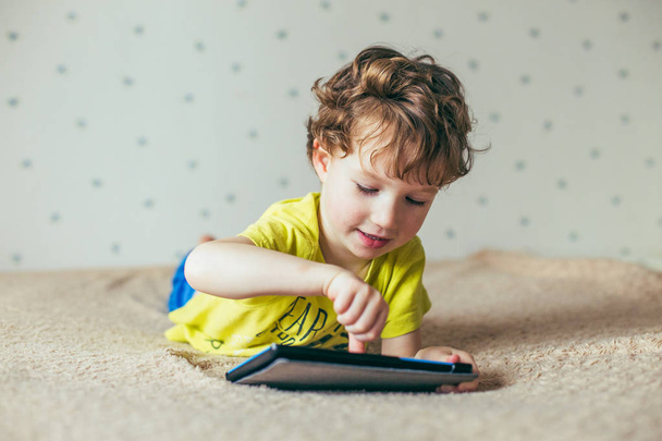 Little cute boy in a green T-shirt playing games on a tablet and watching cartoons - Photo, image