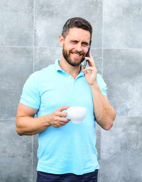 Reasons entrepreneurs drink coffee. Man drink cappuccino speak phone grey wall background. Even if you drink coffee on the go each sip is little break in your day and little moment of self care - Foto, Bild