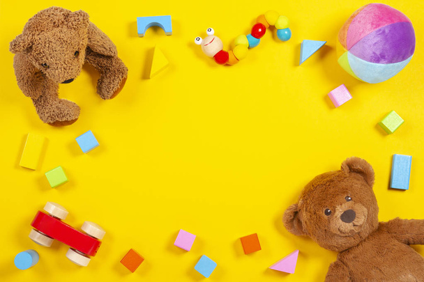 Baby kids toys frame with teddy bear, wooden toy car, colorful bricks on yellow background. Top view - Photo, Image