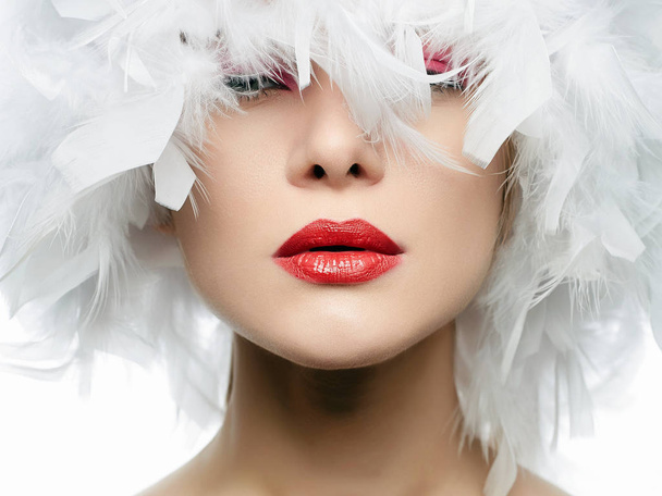 Retrato de Beautiful Girl en plumas blancas. mujer sexy joven con labios rojos, sombrero de plumas, primer plano. Maquillaje de belleza
 - Foto, Imagen
