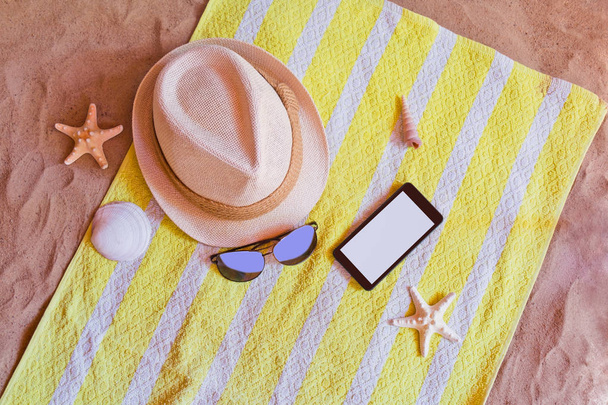 Smartphone, καπέλο και γυαλιά ηλίου για πετσέτα στην παραλία με άμμο - Φωτογραφία, εικόνα
