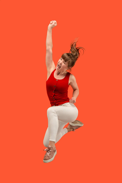 Freedom in moving. Pretty young woman jumping against orange background - Foto, Imagem