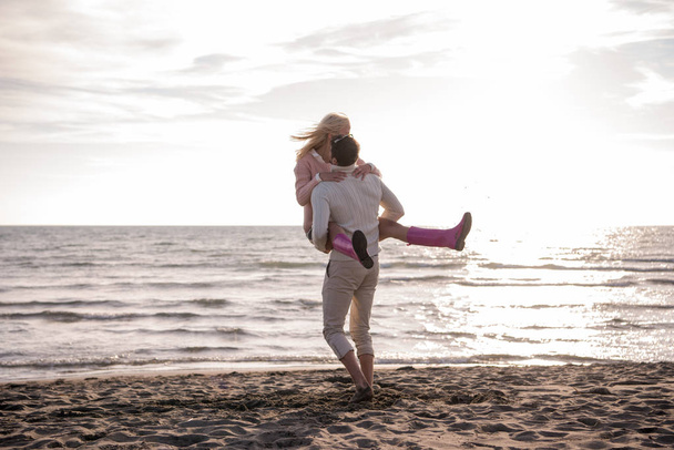Young couple having fun walking and hugging on beach during autumn sunny day - Foto, imagen