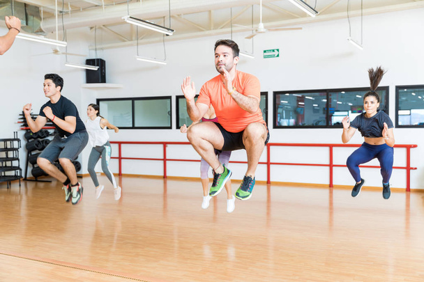 Male and female clients doing tuck jumps on hardwood floor in gym - Photo, Image