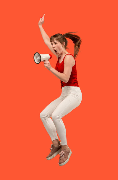 Mulher bonita pulando com megafone isolado sobre fundo vermelho
 - Foto, Imagem