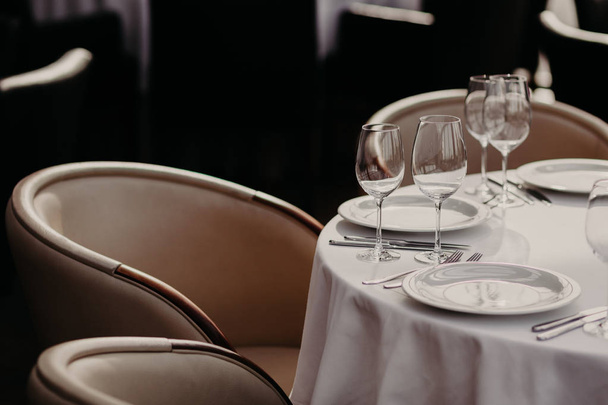 Cubertería y copas de vino sobre mantel blanco, sillones vacíos cerca. Salón de banquetes en el restaurante. Mesa servida para invitados en la cafetería. Concepto de celebración
 - Foto, Imagen