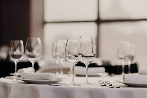 Catering en feest concept. Feestelijke geserveerd diner tafel met glazen en bestek op witte tablewear in luxe feestzaal met geen mensen. De instelling van de tabel - Foto, afbeelding