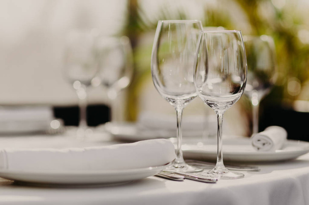 Celebration and dinner concept. Indoor shot of empty wineglasses with empty plates served for guests in restaurant. Festive event. Blurred background. - Φωτογραφία, εικόνα