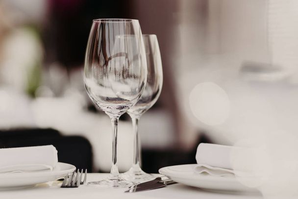 Empty glasses stand near plates and forks on banquet table decorated with white tablewear. Festively served table against blurred background in restaurant - Foto, Bild