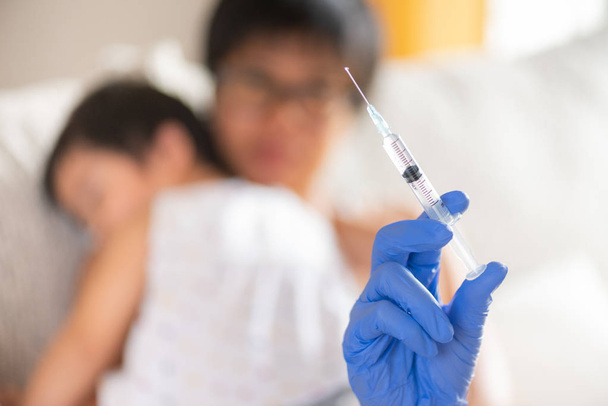 Médico administrando una vacuna inyectable a una niña. Niña con su madre en el fondo
. - Foto, Imagen