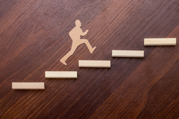 Cut outs of paper man climbing the steps to success in a conceptual image over wooden background. - Fotografie, Obrázek
