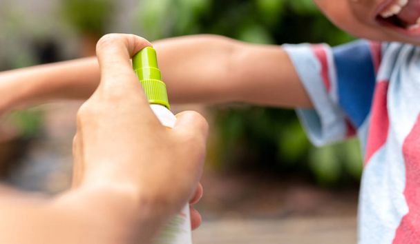 Father spraying insect repellents on his son arm in the garden. - Photo, Image