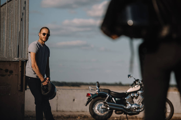 мужчина держит шлем и глядя на подругу, классический мотоцикл рядом
 - Фото, изображение