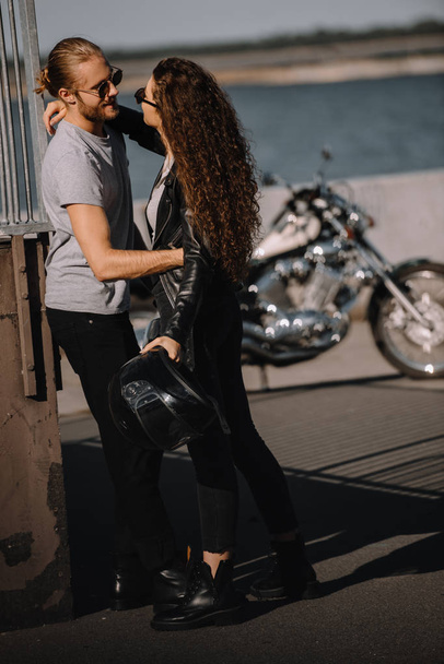 feliz pareja de ciclistas abrazándose en la ciudad con la motocicleta en el fondo
 - Foto, Imagen