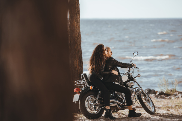 couple in black leather jackets sitting on vintage motorbike and looking at sea - Photo, Image