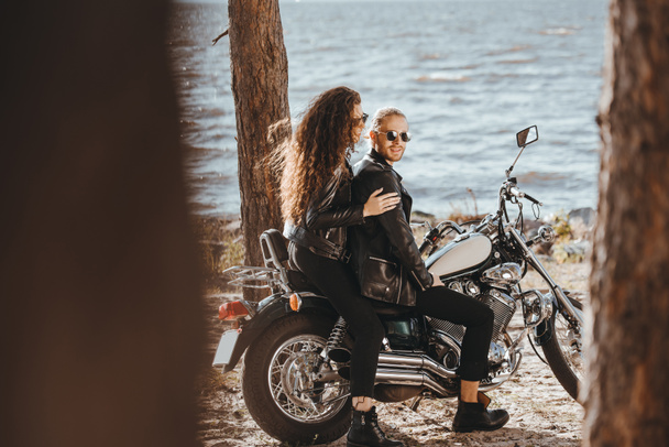 junges Biker-Paar in schwarzen Lederjacken sitzt auf Chopper-Motorrad am Strand - Foto, Bild