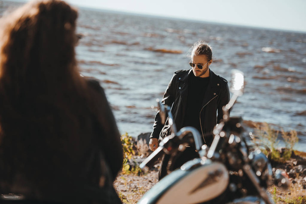 selective focus of woman sitting on motorbike and looking at boyfriend walking on seashore  - Фото, изображение